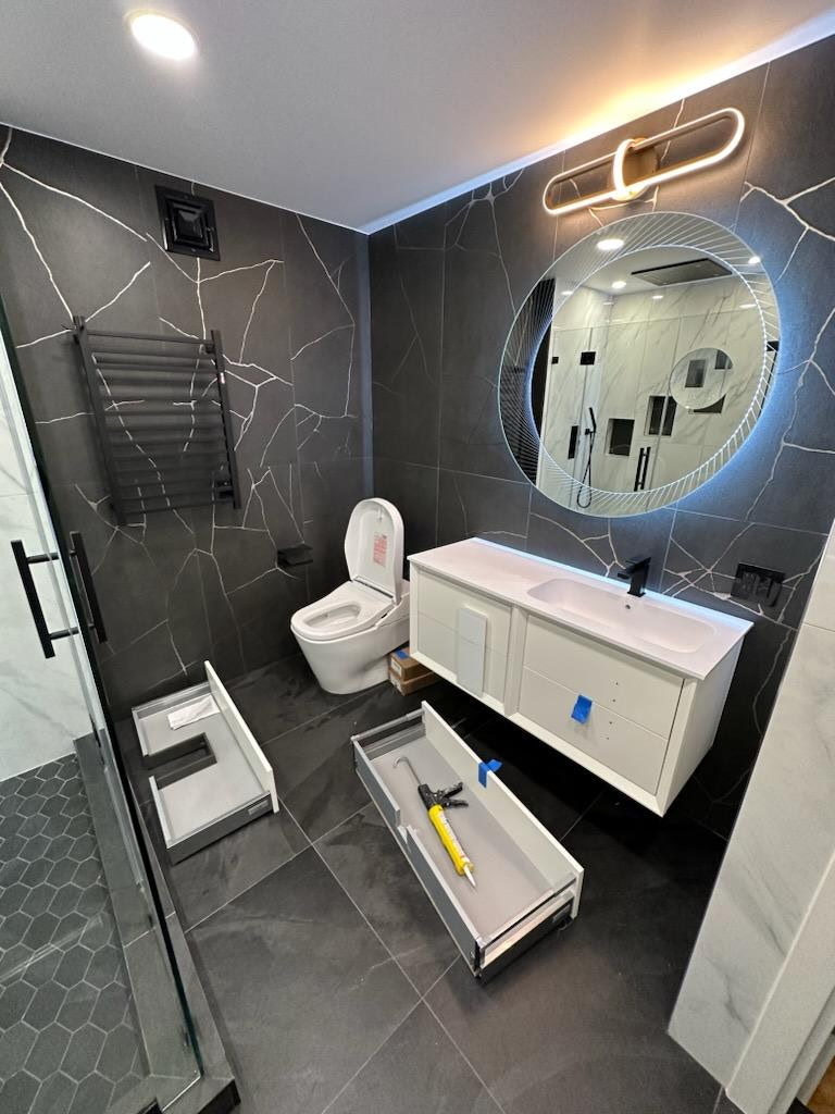 Charcoal marble-look porcelain bathroom with a round backlit mirror, wide white floating vanity and black hardware