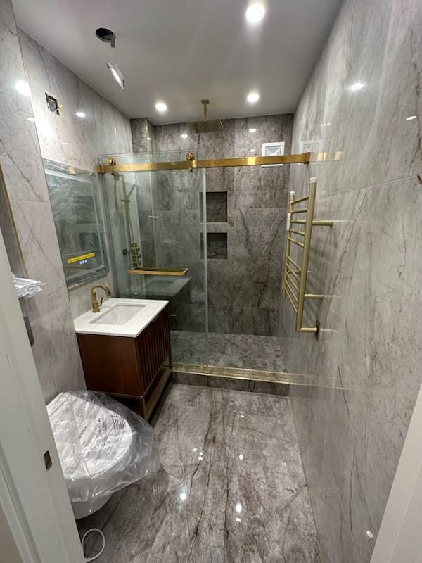Bathroom clad in grey veined marble-look porcelain with brushed gold shower hardware, sliding glass door and walnut vanity
