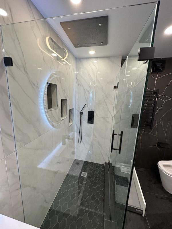 Walk-in shower in white marble-look porcelain with frameless glass, rainfall ceiling shower, built-in bench and recessed niches