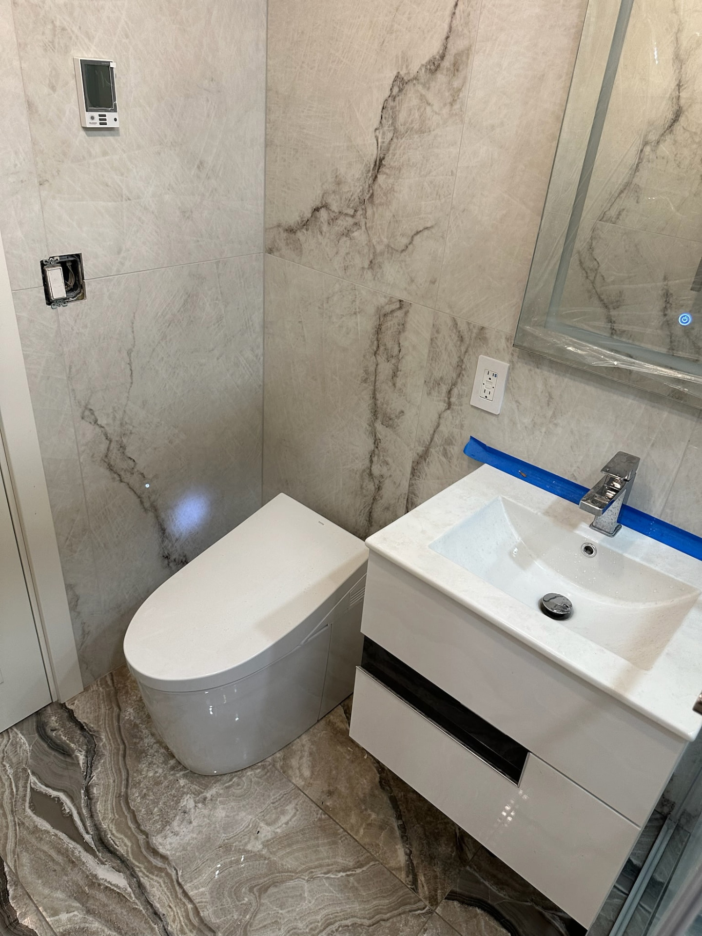 Powder room in soft grey quartzite-look porcelain with a wall-hung smart toilet, gloss white vanity and LED mirror