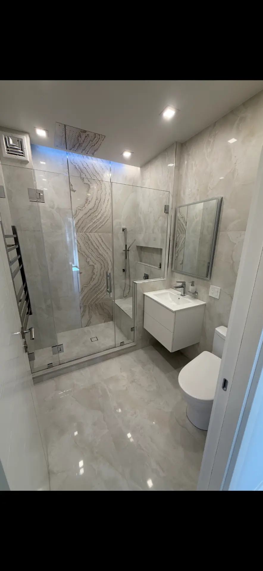 Guest bathroom with book-matched onyx-look porcelain shower wall, frameless glass door, floating white vanity and chrome fixtures